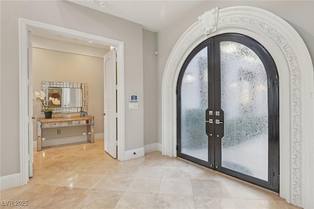 tiled entrance foyer featuring french doors, arched walkways, and baseboards