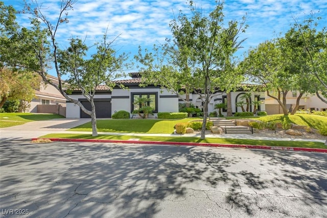 view of front facade with stucco siding, a front lawn, driveway, a garage, and a tiled roof