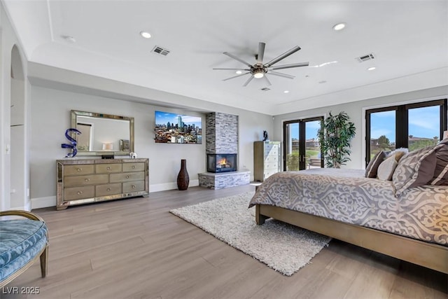 bedroom featuring access to exterior, visible vents, a multi sided fireplace, french doors, and wood finished floors