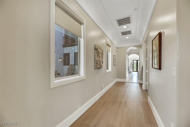 hall with light wood-type flooring, visible vents, arched walkways, and baseboards