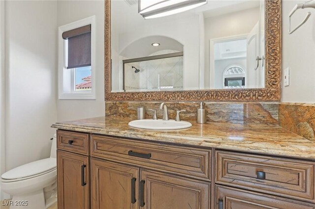 bathroom featuring vanity, toilet, a shower with shower door, and tasteful backsplash