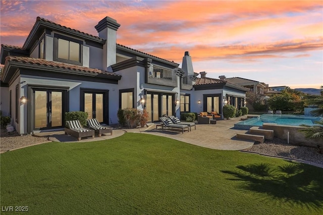 back house at dusk with a yard, a balcony, a patio, and french doors