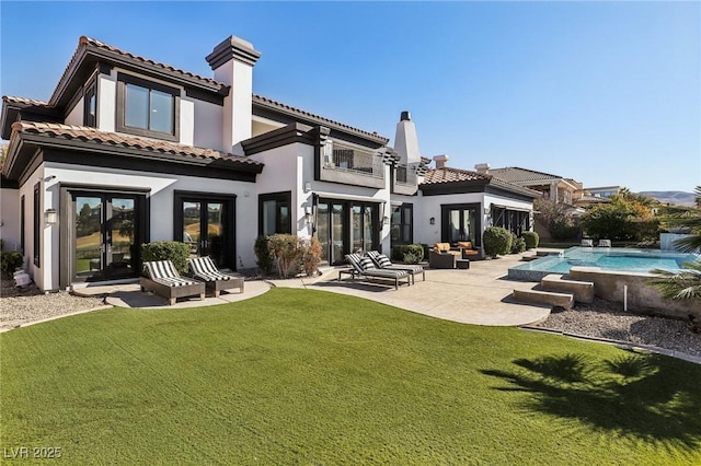 rear view of property featuring a lawn, french doors, a balcony, a patio area, and an outdoor pool