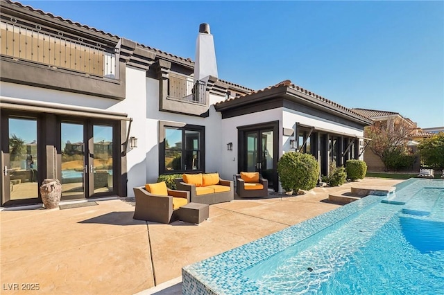 back of property with an outdoor hangout area, a chimney, a balcony, a patio area, and an outdoor pool