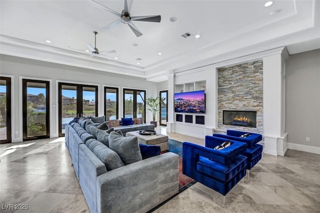 living room with ceiling fan, a stone fireplace, a tray ceiling, and french doors