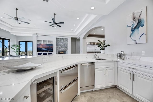 kitchen with a sink, a tray ceiling, open floor plan, wine cooler, and light stone countertops