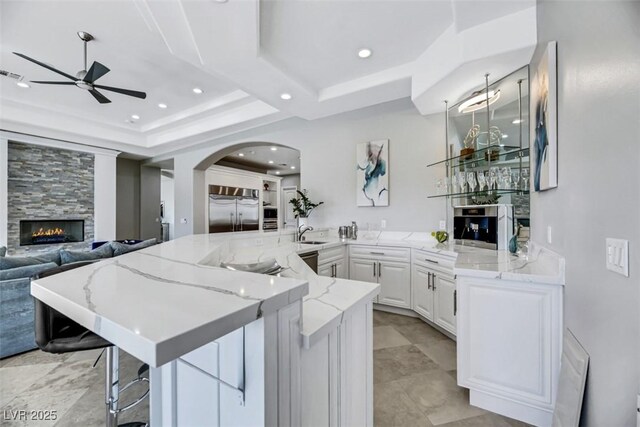 kitchen featuring stainless steel built in refrigerator, kitchen peninsula, a tiled fireplace, a breakfast bar, and white cabinets