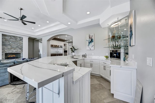 kitchen featuring a ceiling fan, arched walkways, a sink, built in fridge, and open floor plan