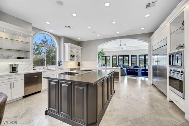 kitchen featuring ceiling fan, a center island, sink, built in appliances, and dark brown cabinets