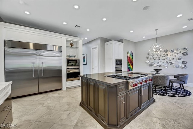 kitchen featuring pendant lighting, white cabinets, built in appliances, dark brown cabinetry, and a chandelier