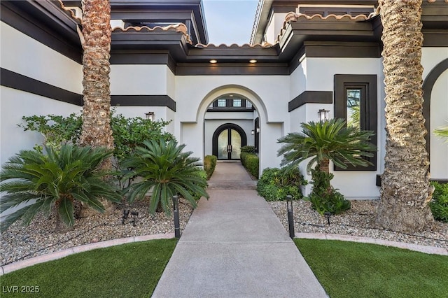 view of exterior entry featuring french doors, a tile roof, and stucco siding