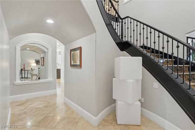 stairs with arched walkways, recessed lighting, lofted ceiling, and baseboards