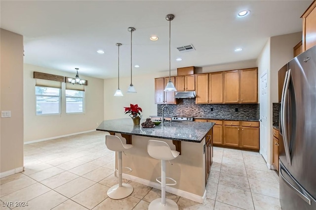 kitchen with stainless steel refrigerator, dark stone countertops, a chandelier, pendant lighting, and a center island with sink