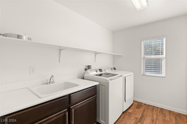 clothes washing area featuring washing machine and dryer, cabinets, sink, and hardwood / wood-style floors