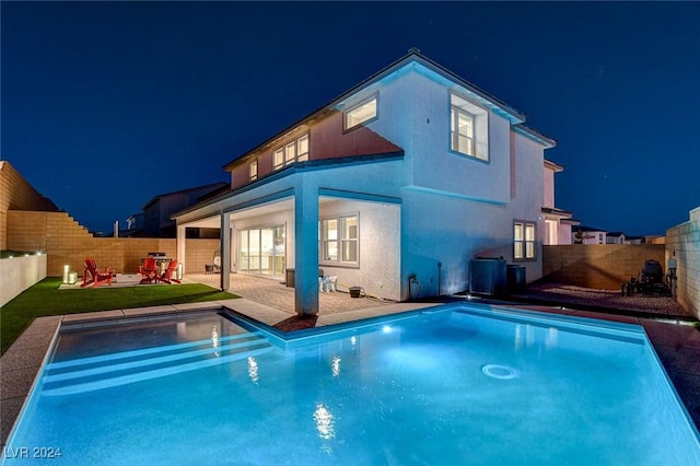 back house at twilight with cooling unit, a fenced in pool, and a patio