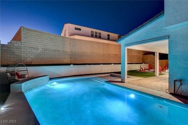 pool at night featuring pool water feature and a patio area