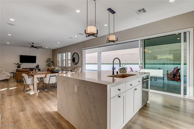 kitchen with light wood-type flooring, ceiling fan, decorative light fixtures, a center island with sink, and white cabinets