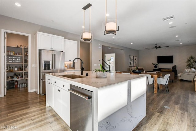 kitchen featuring light stone counters, stainless steel appliances, decorative light fixtures, white cabinetry, and an island with sink