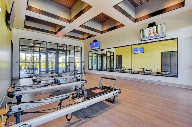 gym featuring wood-type flooring, coffered ceiling, and a high ceiling