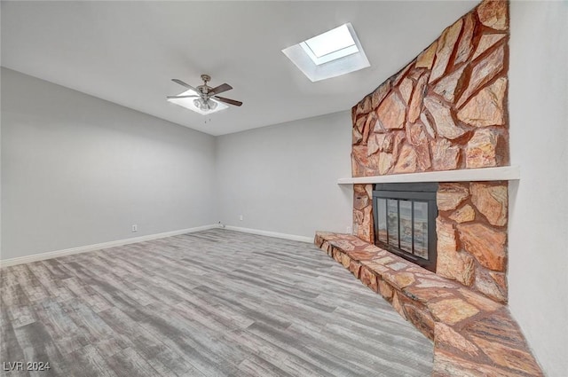 unfurnished living room featuring vaulted ceiling with skylight, ceiling fan, a fireplace, and hardwood / wood-style flooring