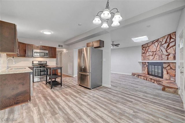 kitchen with sink, a fireplace, appliances with stainless steel finishes, ceiling fan with notable chandelier, and light wood-type flooring