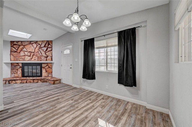 interior space featuring a chandelier, hardwood / wood-style floors, a stone fireplace, and vaulted ceiling with skylight