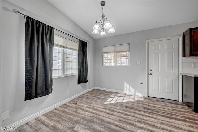 unfurnished dining area featuring a chandelier, light hardwood / wood-style flooring, and vaulted ceiling