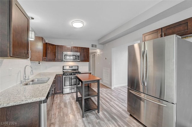 kitchen with light stone countertops, appliances with stainless steel finishes, vaulted ceiling, sink, and light hardwood / wood-style floors