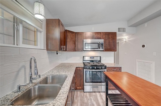 kitchen with backsplash, sink, light stone countertops, appliances with stainless steel finishes, and light hardwood / wood-style floors