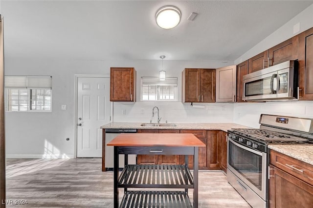 kitchen featuring tasteful backsplash, light stone counters, stainless steel appliances, sink, and decorative light fixtures