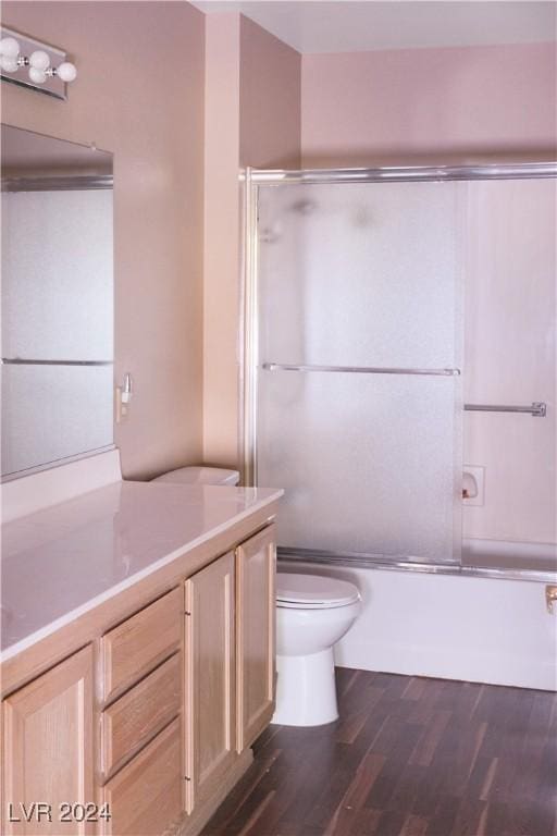 full bathroom with hardwood / wood-style flooring, vanity, toilet, and bath / shower combo with glass door