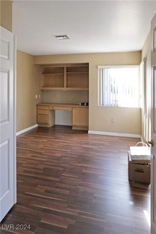 unfurnished living room with built in desk and dark wood-type flooring