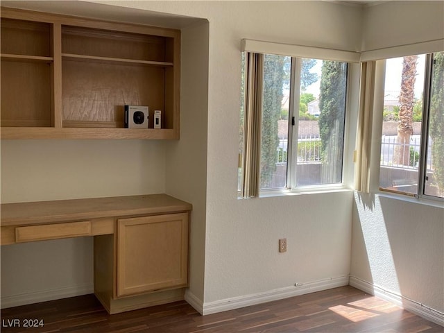 unfurnished dining area with dark wood-type flooring, built in desk, and baseboards