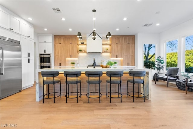 kitchen featuring hanging light fixtures, light hardwood / wood-style flooring, an island with sink, white cabinets, and appliances with stainless steel finishes