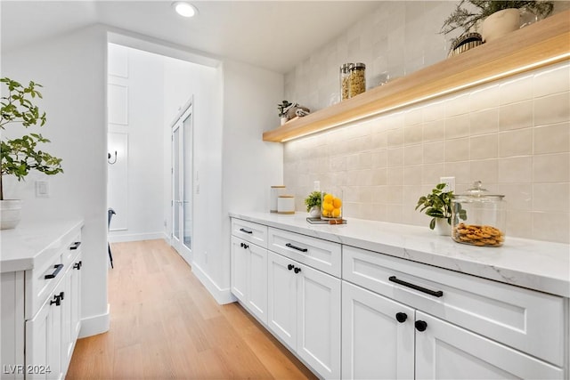 bar featuring light wood-type flooring, tasteful backsplash, white cabinetry, and light stone counters