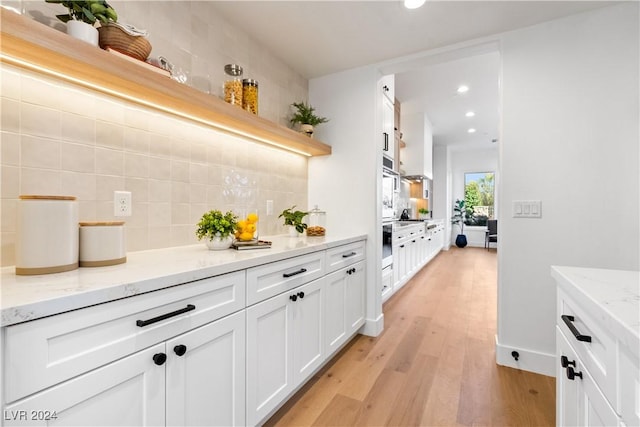 bar with decorative backsplash, light stone counters, white cabinetry, and light hardwood / wood-style flooring