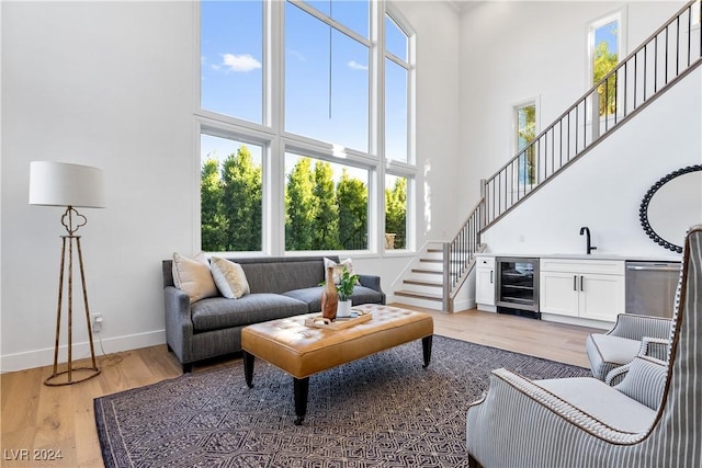 living room with wine cooler, light hardwood / wood-style flooring, a high ceiling, and indoor wet bar