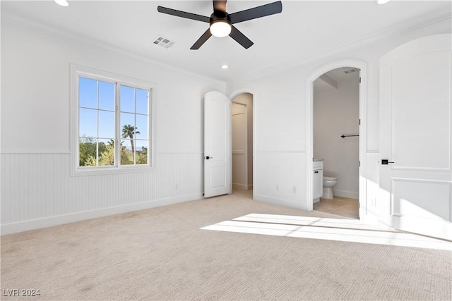 unfurnished bedroom featuring ceiling fan, light colored carpet, crown molding, and connected bathroom