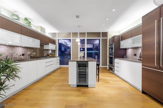 kitchen with pendant lighting, wine cooler, decorative backsplash, light wood-type flooring, and a kitchen island