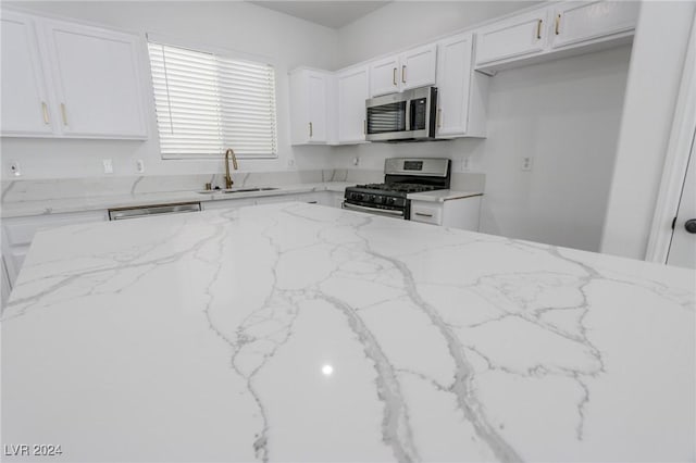 kitchen with white cabinets, appliances with stainless steel finishes, light stone counters, and sink