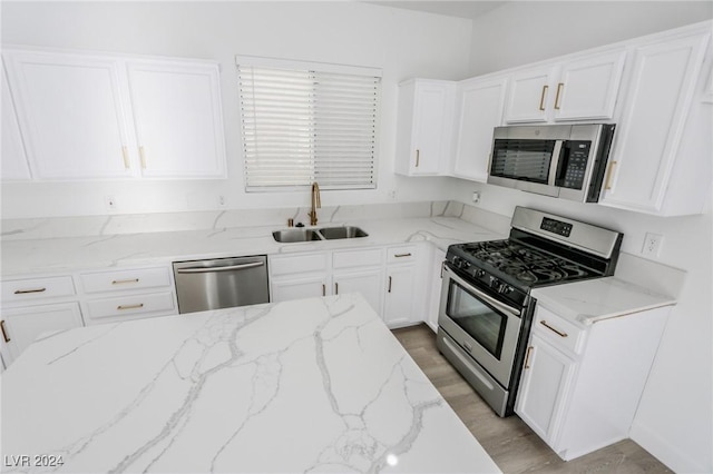 kitchen with light stone countertops, sink, light hardwood / wood-style floors, white cabinets, and appliances with stainless steel finishes