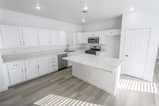 kitchen with light wood-type flooring, stainless steel appliances, sink, white cabinets, and a center island