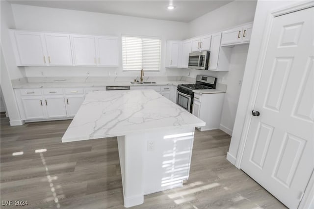 kitchen with a center island, white cabinets, sink, light stone countertops, and appliances with stainless steel finishes