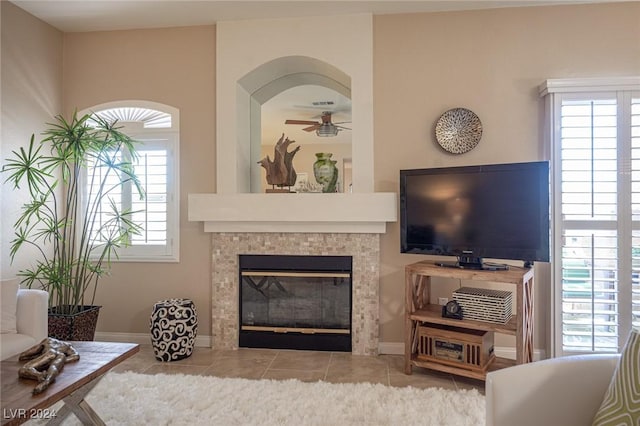 tiled living room with ceiling fan, a wealth of natural light, and a tiled fireplace