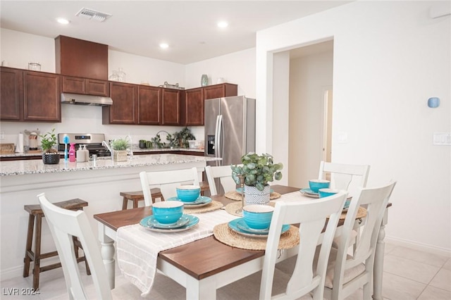 kitchen featuring a kitchen breakfast bar, light stone counters, dark brown cabinets, stainless steel appliances, and light tile patterned floors