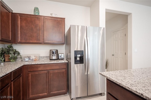 kitchen featuring light stone countertops, stainless steel fridge with ice dispenser, dark brown cabinetry, and light tile patterned floors