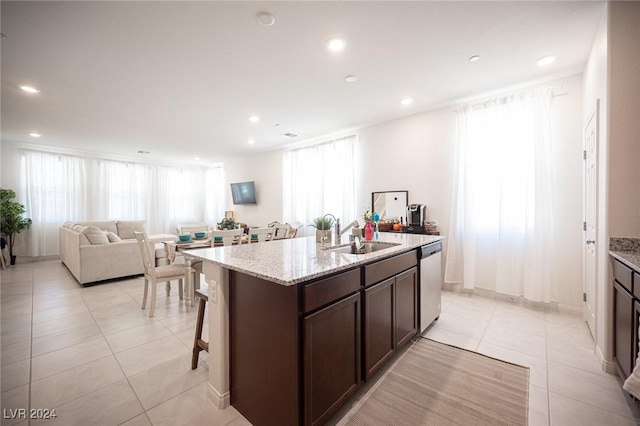 kitchen featuring a kitchen island with sink, sink, stainless steel dishwasher, light stone countertops, and dark brown cabinetry