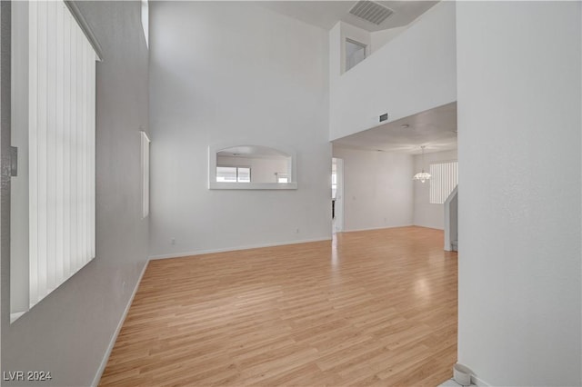 unfurnished living room featuring light hardwood / wood-style flooring, a towering ceiling, and an inviting chandelier