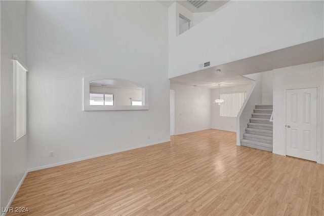 unfurnished living room featuring light wood-type flooring, a high ceiling, and an inviting chandelier