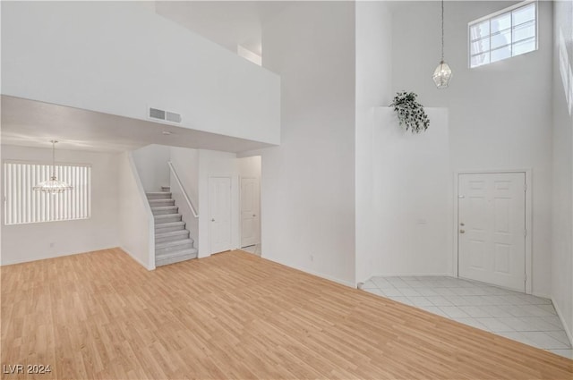 unfurnished living room with a chandelier, a towering ceiling, and light hardwood / wood-style floors